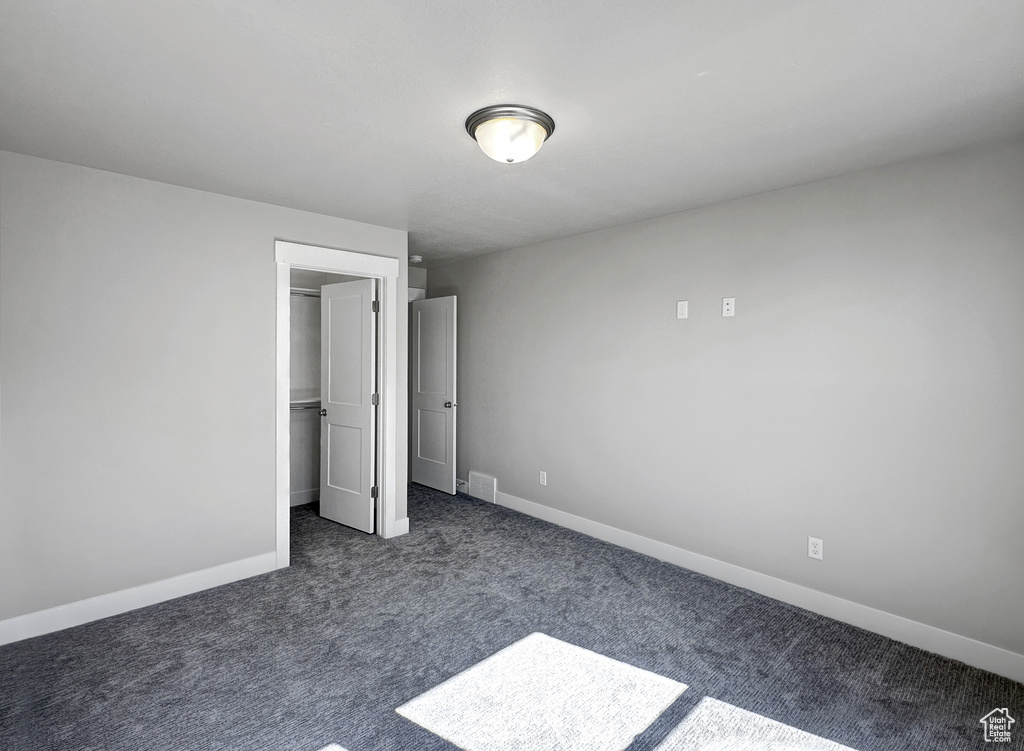 Unfurnished bedroom featuring dark colored carpet, a closet, and a walk in closet