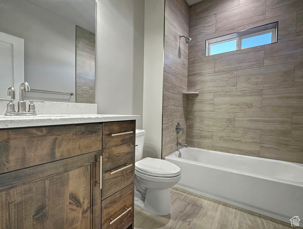 Full bathroom featuring hardwood / wood-style floors, tiled shower / bath, vanity, and toilet