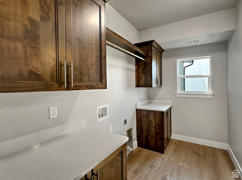 Washroom with electric dryer hookup, light wood-type flooring, hookup for a washing machine, and cabinets