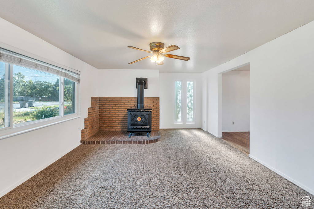 Unfurnished living room with a wood stove, carpet, and ceiling fan