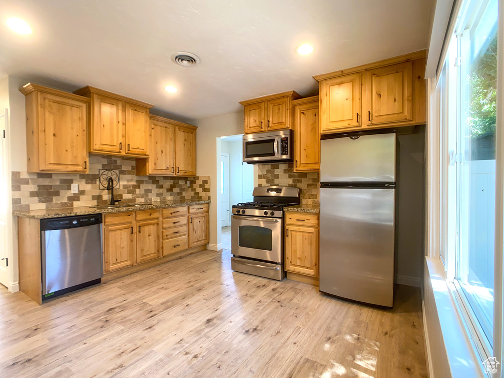 Kitchen with stainless steel appliances, decorative backsplash, sink, light stone countertops, and light hardwood / wood-style flooring