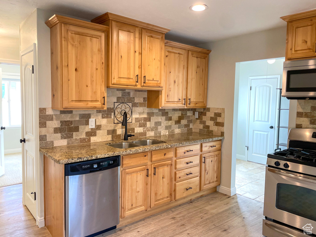 Kitchen with light hardwood / wood-style flooring, light stone countertops, appliances with stainless steel finishes, decorative backsplash, and sink