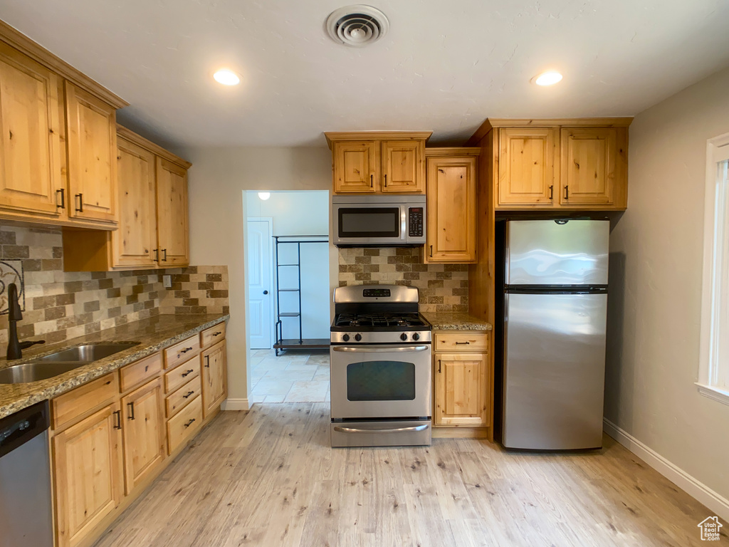 Kitchen featuring light hardwood / wood-style flooring, stainless steel appliances, decorative backsplash, stone counters, and sink