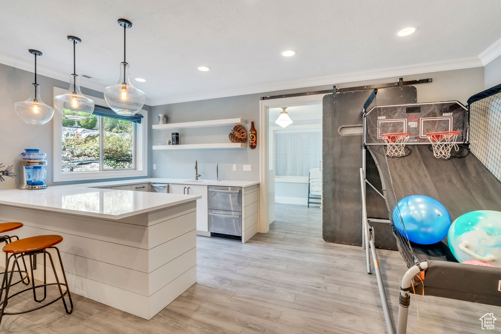 Kitchen featuring white cabinetry, crown molding, a barn door, light hardwood / wood-style floors, and a kitchen breakfast bar