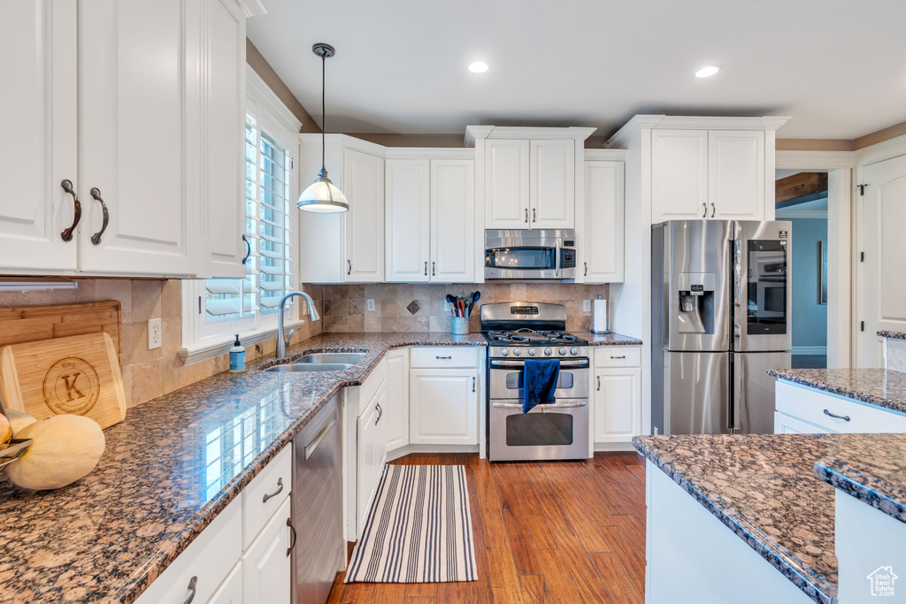 Kitchen with white cabinetry, hardwood / wood-style floors, sink, appliances with stainless steel finishes, and backsplash