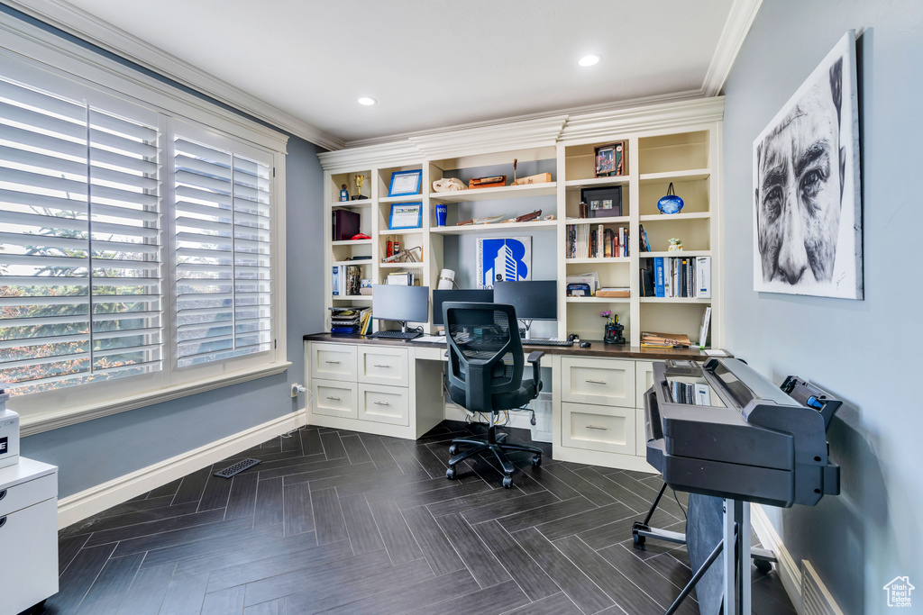 Office space with dark parquet flooring, built in desk, and crown molding