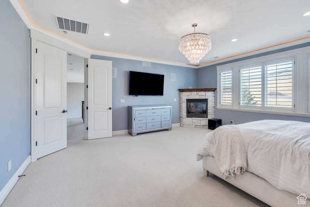 Bedroom with a stone fireplace, light carpet, crown molding, and an inviting chandelier