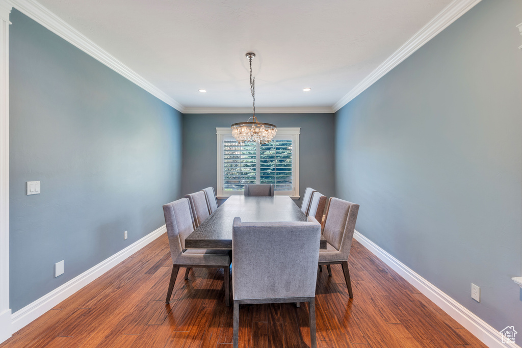 Dining room with dark wood-type flooring, a chandelier, and ornamental molding