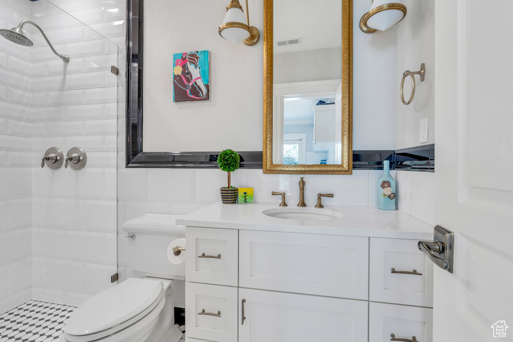 Bathroom featuring tiled shower, toilet, vanity, tile walls, and decorative backsplash