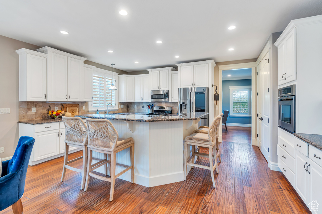 Kitchen featuring a breakfast bar, appliances with stainless steel finishes, tasteful backsplash, and hardwood / wood-style flooring