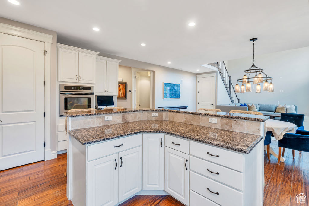 Kitchen featuring dark stone counters, wood-type flooring, stainless steel oven, and white cabinets