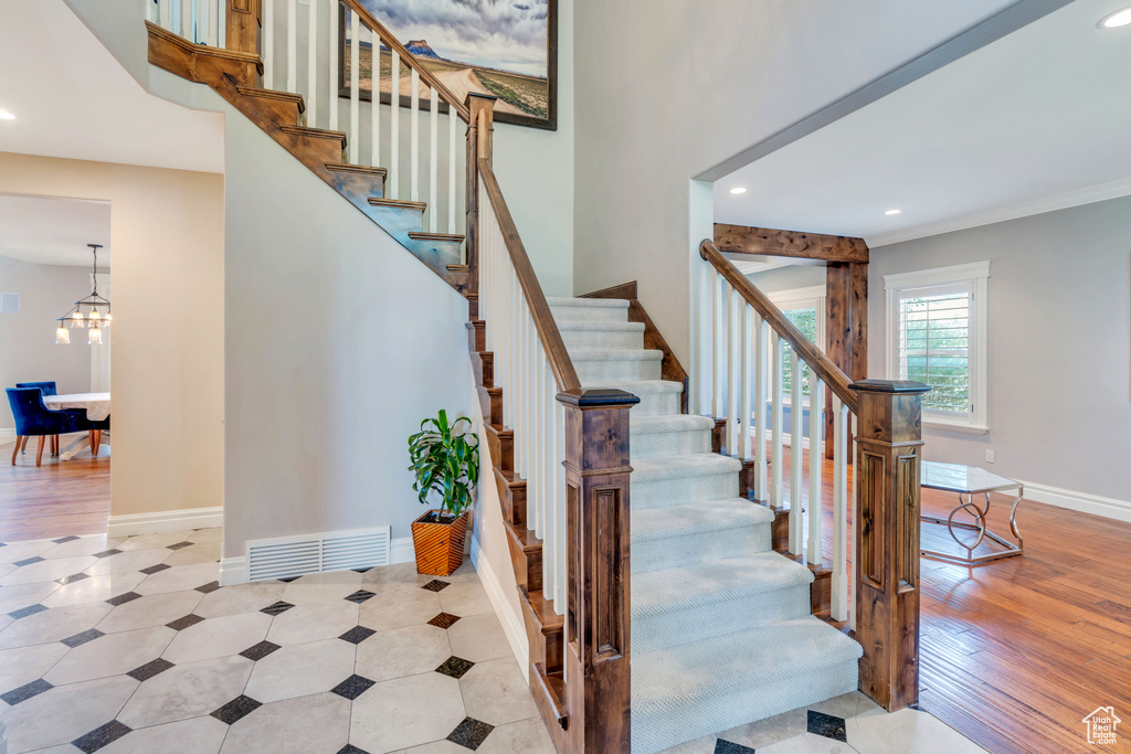 Stairway featuring a notable chandelier, light wood-type flooring, and ornamental molding