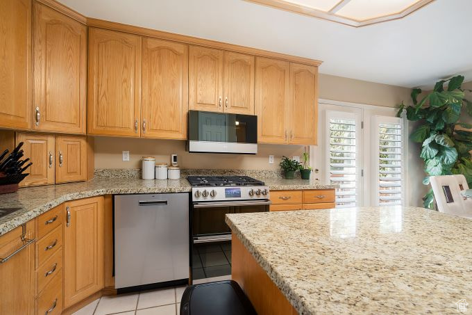 Kitchen with appliances with stainless steel finishes, light tile patterned floors, and light stone countertops