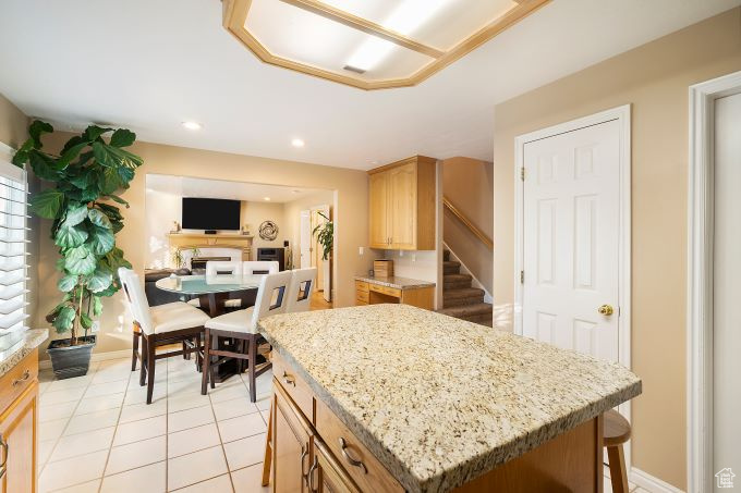 Kitchen featuring light brown cabinetry, light stone countertops, light tile patterned floors, and a kitchen island