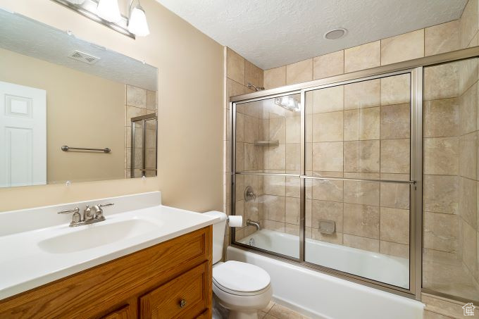 Full bathroom featuring tile patterned flooring, bath / shower combo with glass door, a textured ceiling, toilet, and vanity