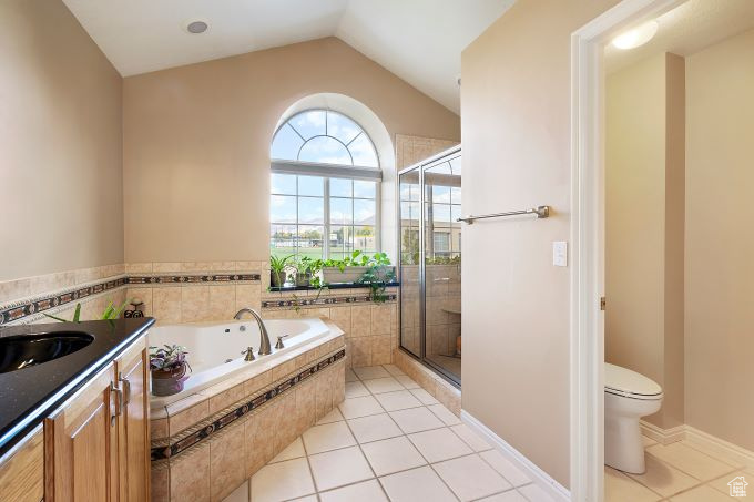 Full bathroom featuring toilet, vanity, tile patterned floors, separate shower and tub, and vaulted ceiling