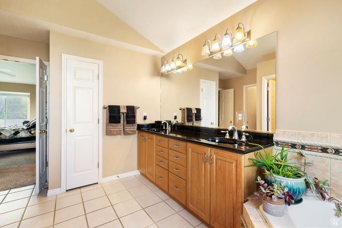 Bathroom featuring a tub, double sink vanity, vaulted ceiling, and tile patterned flooring