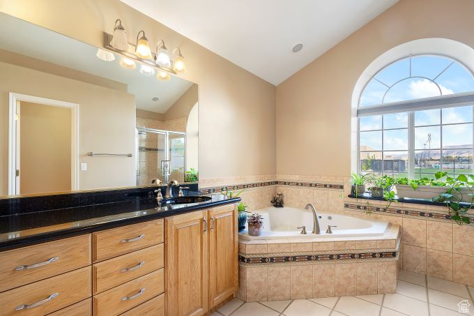 Bathroom with tile patterned flooring, independent shower and bath, vaulted ceiling, and vanity