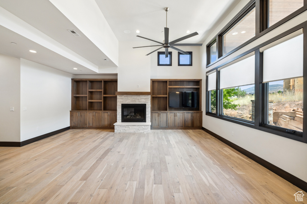 Unfurnished living room with ceiling fan, a fireplace, light hardwood / wood-style flooring, and a high ceiling