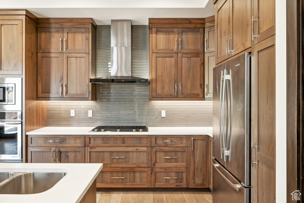 Kitchen featuring tasteful backsplash, light hardwood / wood-style floors, appliances with stainless steel finishes, and wall chimney exhaust hood