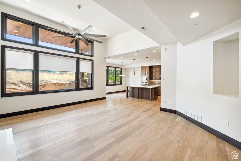 Unfurnished living room with light hardwood / wood-style flooring, ceiling fan, and a towering ceiling