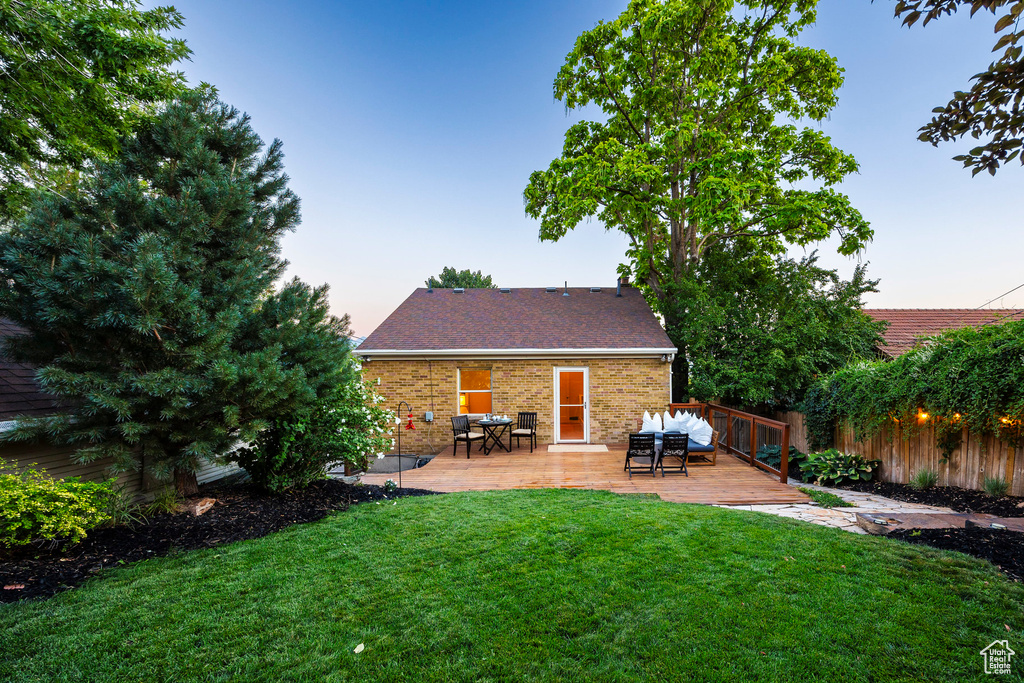 Back house at dusk with a deck and a yard