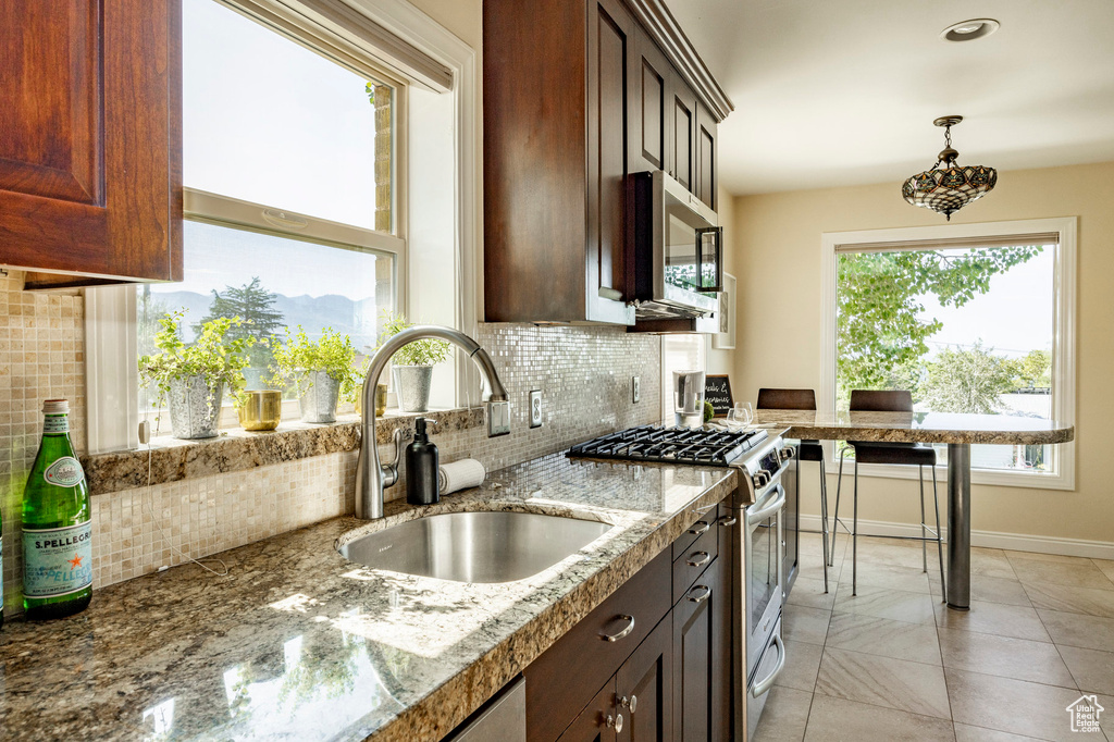 Kitchen with appliances with stainless steel finishes, decorative light fixtures, decorative backsplash, sink, and light tile patterned flooring