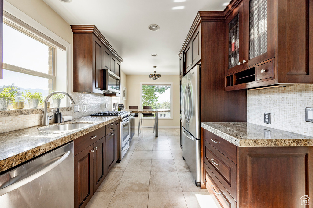 Kitchen featuring appliances with stainless steel finishes, backsplash, sink, pendant lighting, and light tile patterned floors