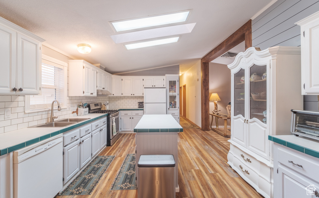 Kitchen with white appliances, sink, a center island, light hardwood / wood-style flooring, and vaulted ceiling with skylight