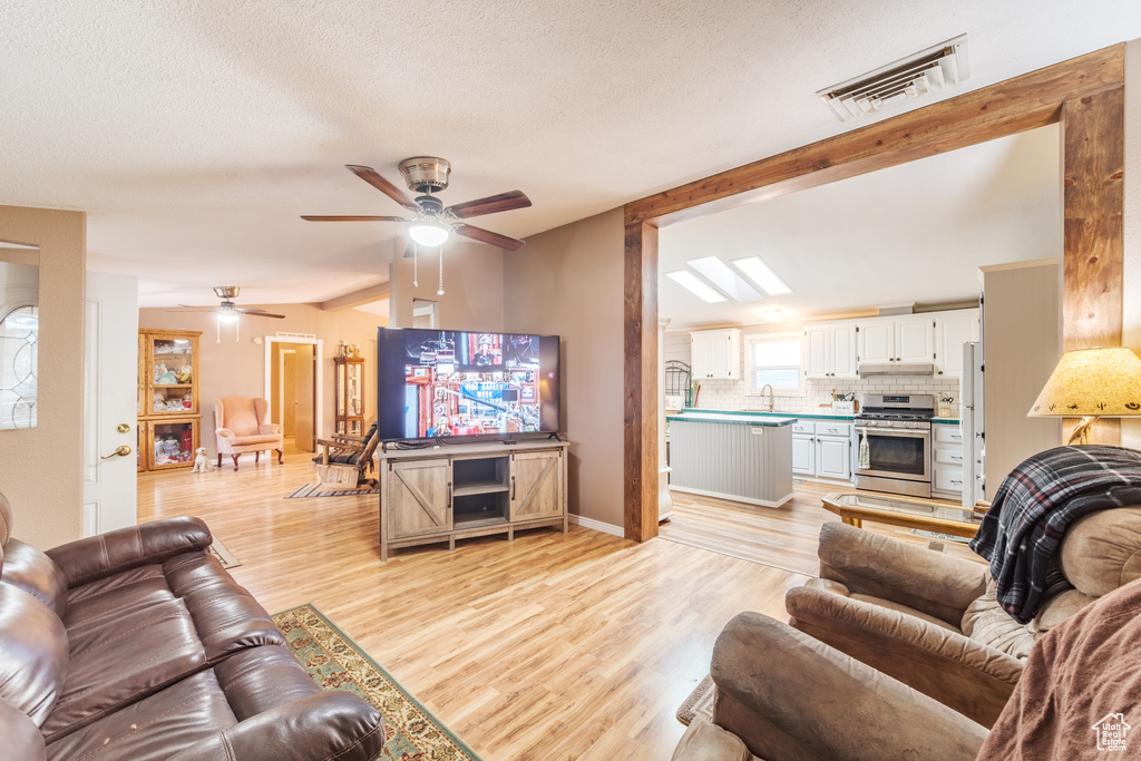 Living room featuring a textured ceiling, ceiling fan, and light wood-type flooring