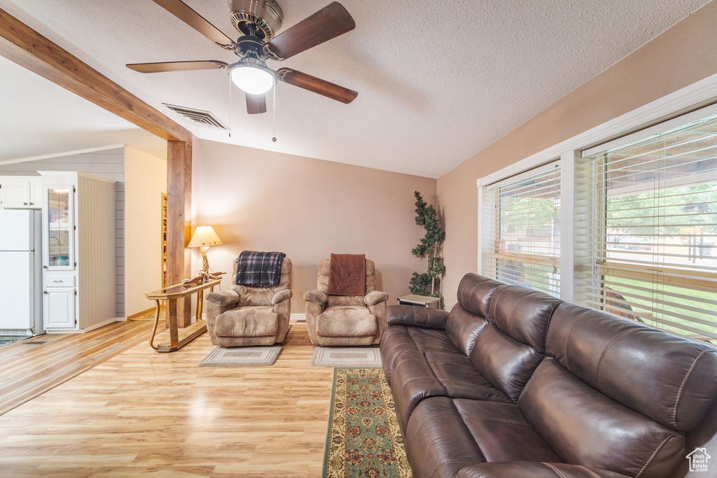 Living room with light hardwood / wood-style floors, a textured ceiling, ceiling fan, and vaulted ceiling with beams