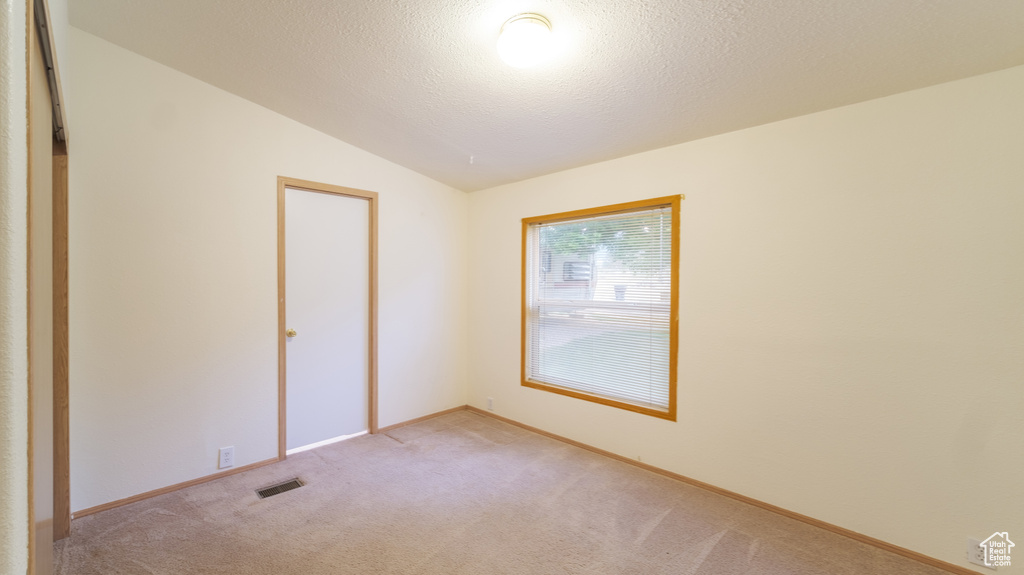 Carpeted spare room featuring a textured ceiling and vaulted ceiling