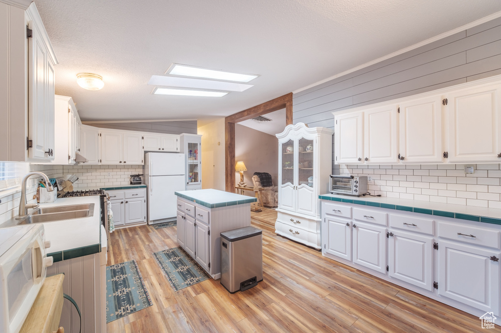 Kitchen featuring white appliances, white cabinets, vaulted ceiling with skylight, light hardwood / wood-style floors, and a kitchen island