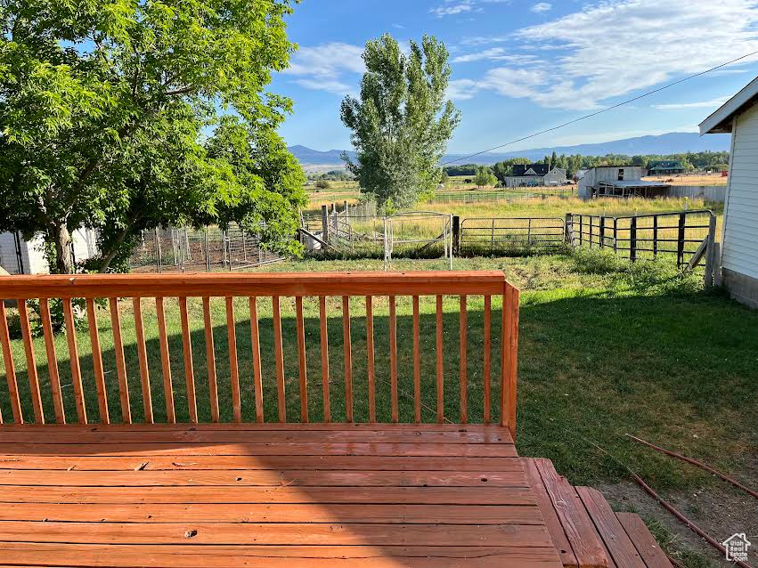 Wooden terrace featuring a mountain view, a rural view, and a yard