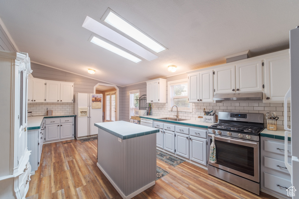 Kitchen with lofted ceiling with skylight, white appliances, light wood-type flooring, white cabinets, and a center island