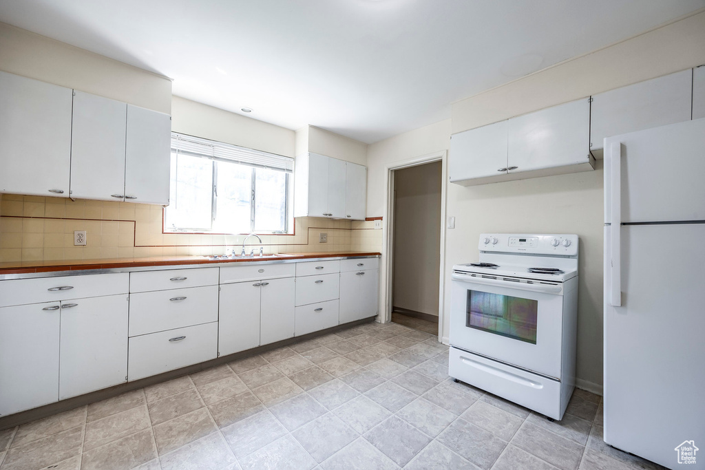 Kitchen with white cabinets, white appliances, backsplash, and light tile patterned floors