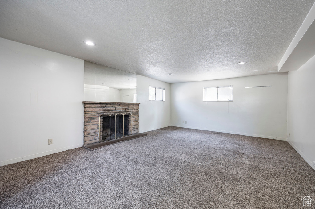 Unfurnished living room with carpet flooring, a textured ceiling, and a stone fireplace