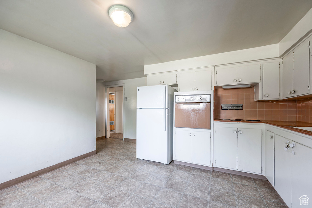 Kitchen featuring white fridge, white cabinetry, tasteful backsplash, oven, and light tile patterned floors