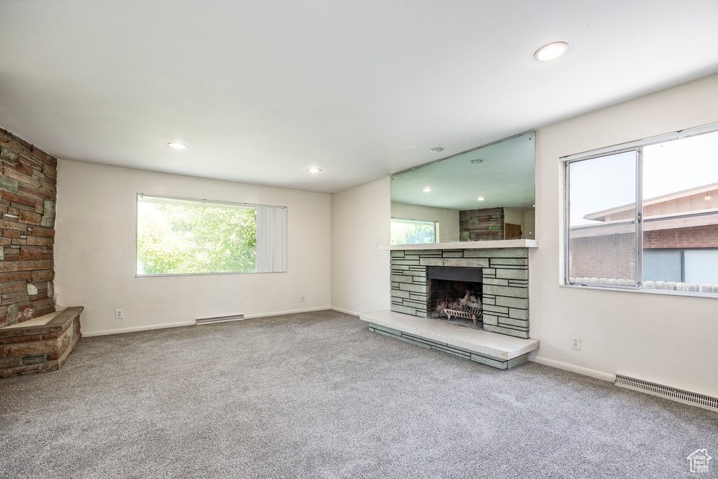 Unfurnished living room with a stone fireplace, a baseboard radiator, and carpet floors