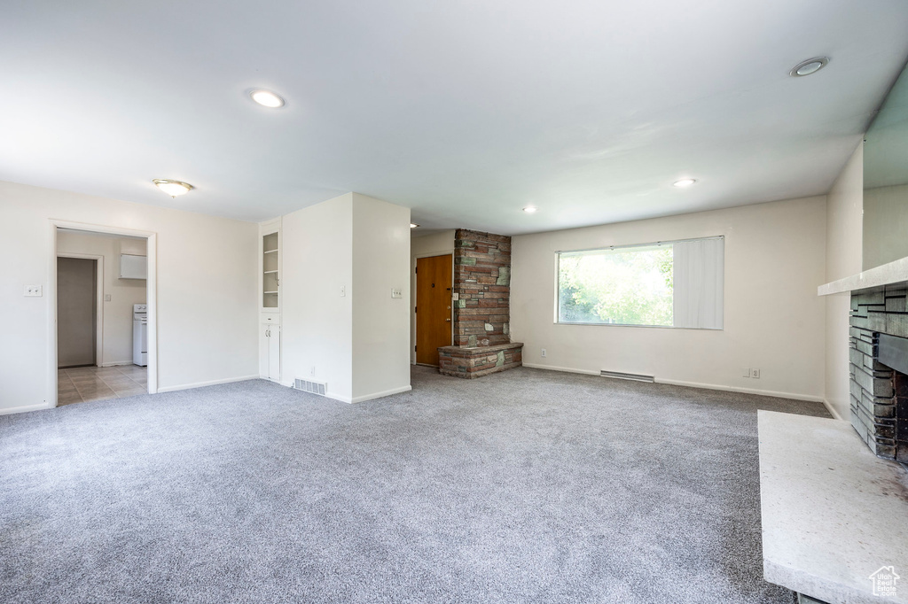 Unfurnished living room featuring a baseboard heating unit, light colored carpet, and brick wall