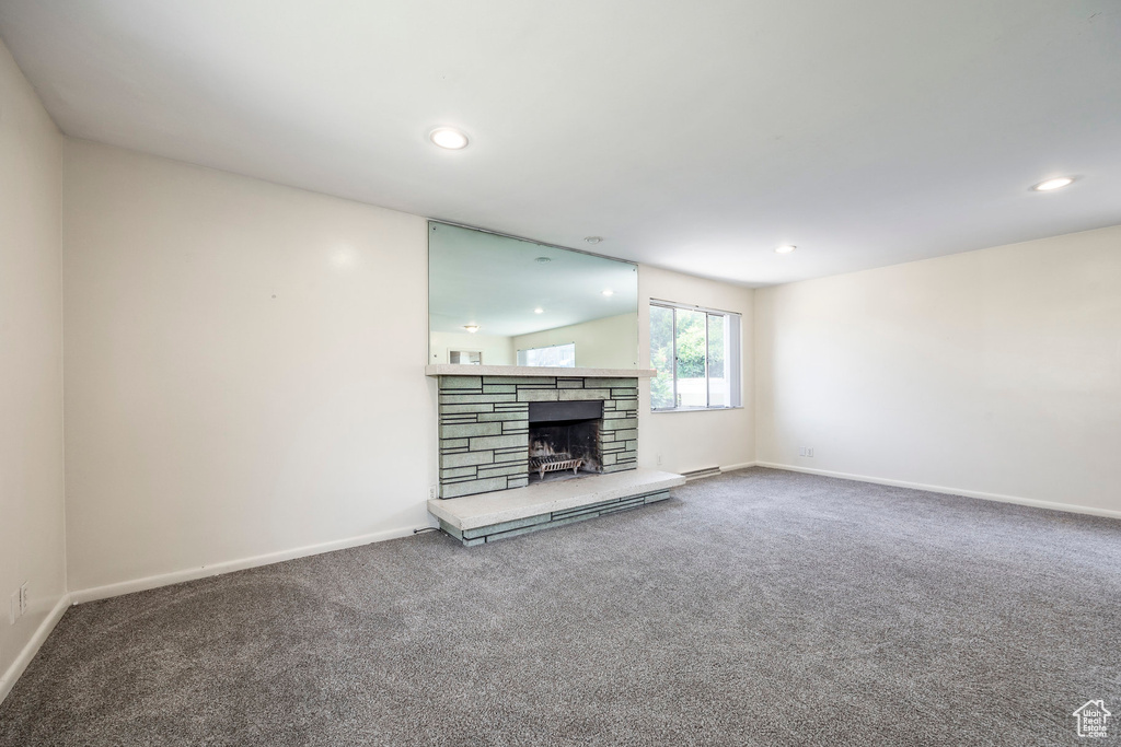 Unfurnished living room with a stone fireplace, lofted ceiling, and carpet floors