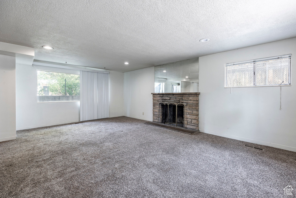 Unfurnished living room featuring a textured ceiling, carpet flooring, and a fireplace