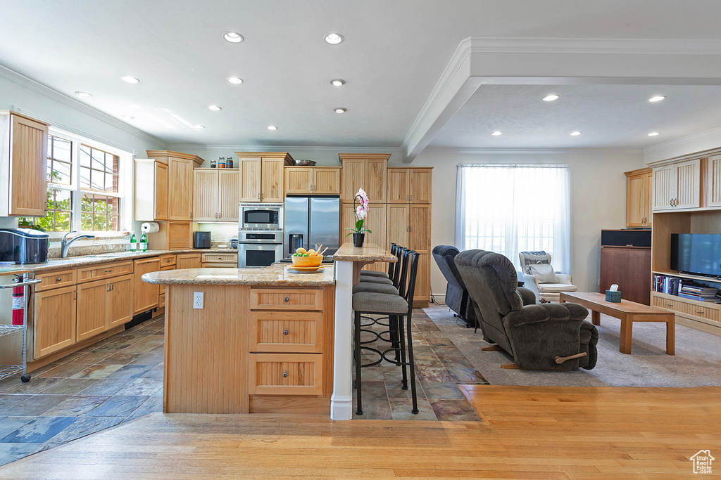 Kitchen with sink, a center island, a breakfast bar area, appliances with stainless steel finishes, and light hardwood / wood-style flooring