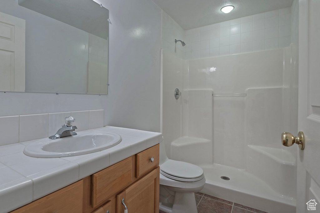 Bathroom featuring tasteful backsplash, tile patterned flooring, toilet, a shower, and vanity