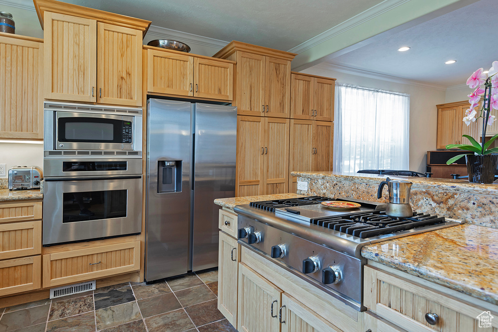 Kitchen featuring light brown cabinetry, light stone counters, dark tile patterned flooring, and stainless steel appliances