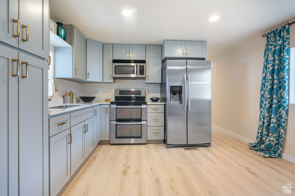 Kitchen with light hardwood / wood-style floors, sink, gray cabinetry, and stainless steel appliances