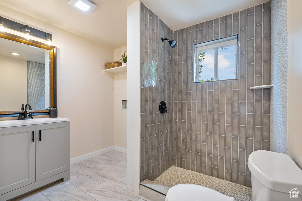 Bathroom featuring tile patterned floors, toilet, vanity, and a tile shower