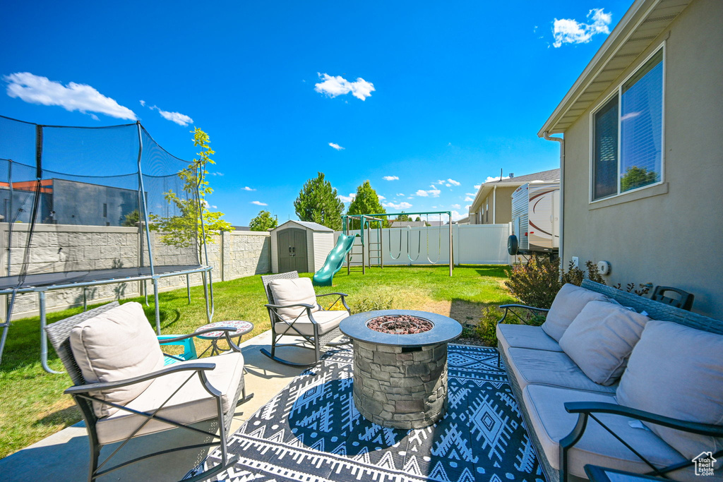 View of patio with a trampoline, a storage unit, an outdoor living space with a fire pit, and a playground