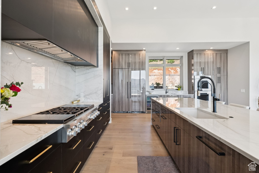 Kitchen featuring modern cabinets, wall chimney range hood, tasteful backsplash, light wood-style flooring, and recessed lighting