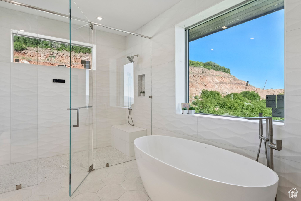 Full bathroom with healthy amount of natural light, a freestanding bath, a shower stall, tile walls, and tile patterned flooring